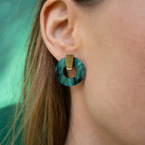 Close-up of a womans ear wearing a hypoallergenic, dark green marbled Minimalist Circle Stud Earring with a gold rectangular accent; her light brown hair partially frames her ear.
