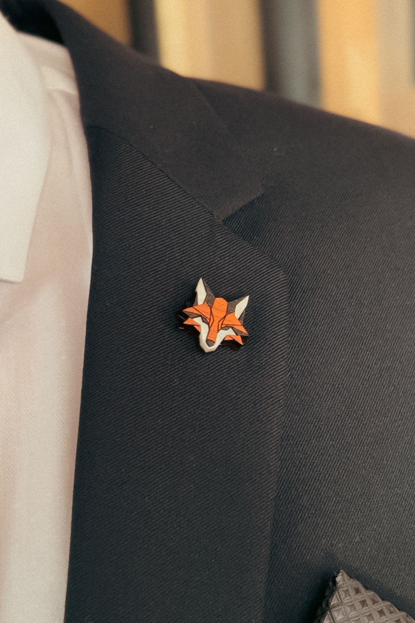 A person wearing a black suit jacket, white shirt, and patterned pocket square, with a geometric Fox Pin made from recycled wood on the lapel—perfect for showcasing eco-conscious style.