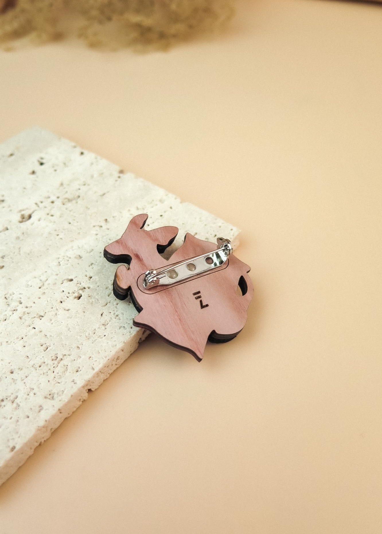 A playful Dachshund brooch in pink lies on a textured white stone surface, set against a beige background.