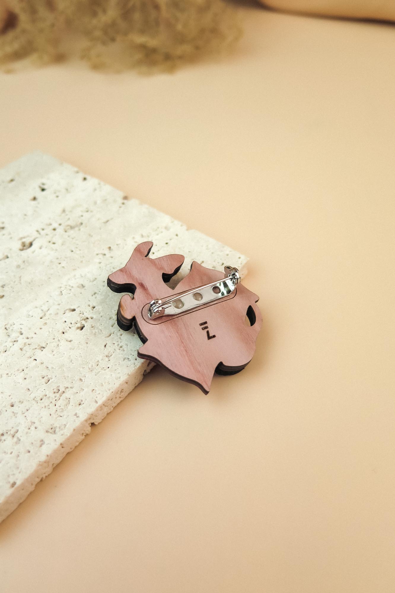 A playful Dachshund brooch in pink lies on a textured white stone surface, set against a beige background.