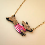 A necklace with a gold chain featuring a pendant shaped like a Dachshund in a colorful sweater, crafted from sustainable wood, set against a light beige background.
