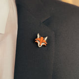 A person wearing a black suit jacket, white shirt, and patterned pocket square, with a geometric Fox Pin made from recycled wood on the lapel—perfect for showcasing eco-conscious style.