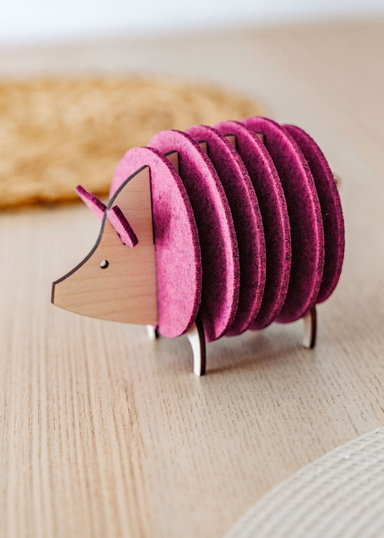A wooden and felt coaster holder shaped like a hedgehog, with pink felt discs forming the body, sits on a light wooden table—a charming housewarming gift for any home.