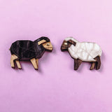 Two small wooden Sheep Badges shaped like sheep, one dark brown and one white, placed on a light purple background—a charming accessory choice for animal lovers.
