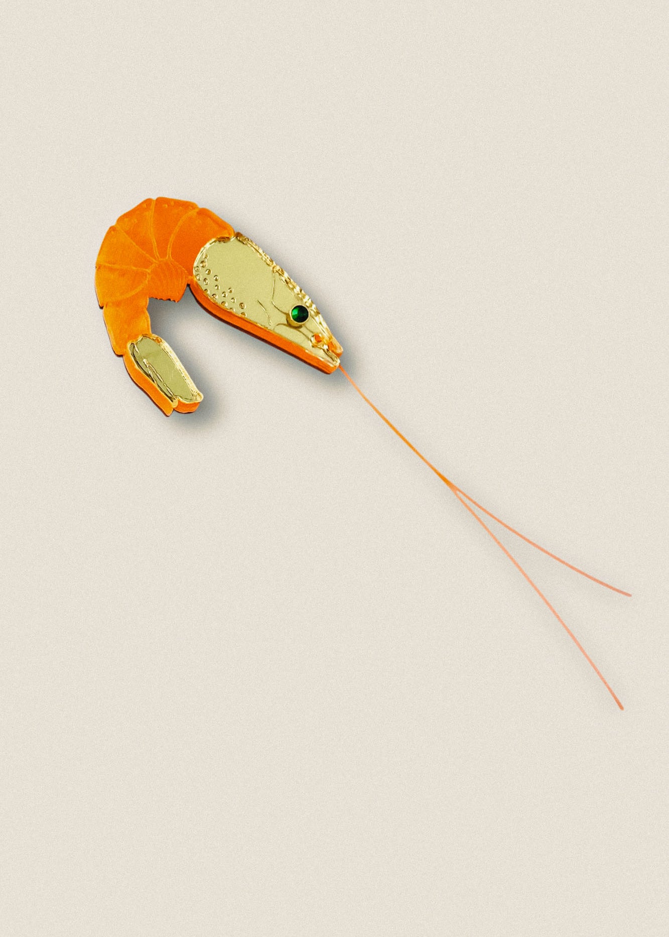 A Shrimp Pin accessory designed to resemble a shrimp, with an orange segmented body and detailed gold head, featuring green and black accent stones and long, thin orange antennae—perfect for adding wardrobe charm against any outfit.