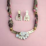A handmade necklace with a fabric-wrapped chain and matching earrings, both featuring white, abstract, acrylic tulip-like pendants, displayed on a pink background.