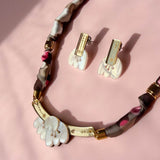 A handmade necklace and matching clip-on earrings with white, acrylic tulip-shaped pendants, gold accents, and a fabric-wrapped brown and pink chain, displayed on a soft pink background.